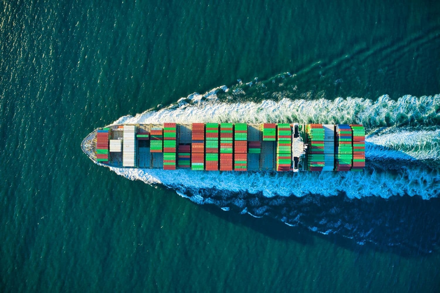 Aerial view of a cargo ship carrying colorful shipping containers across the ocean.