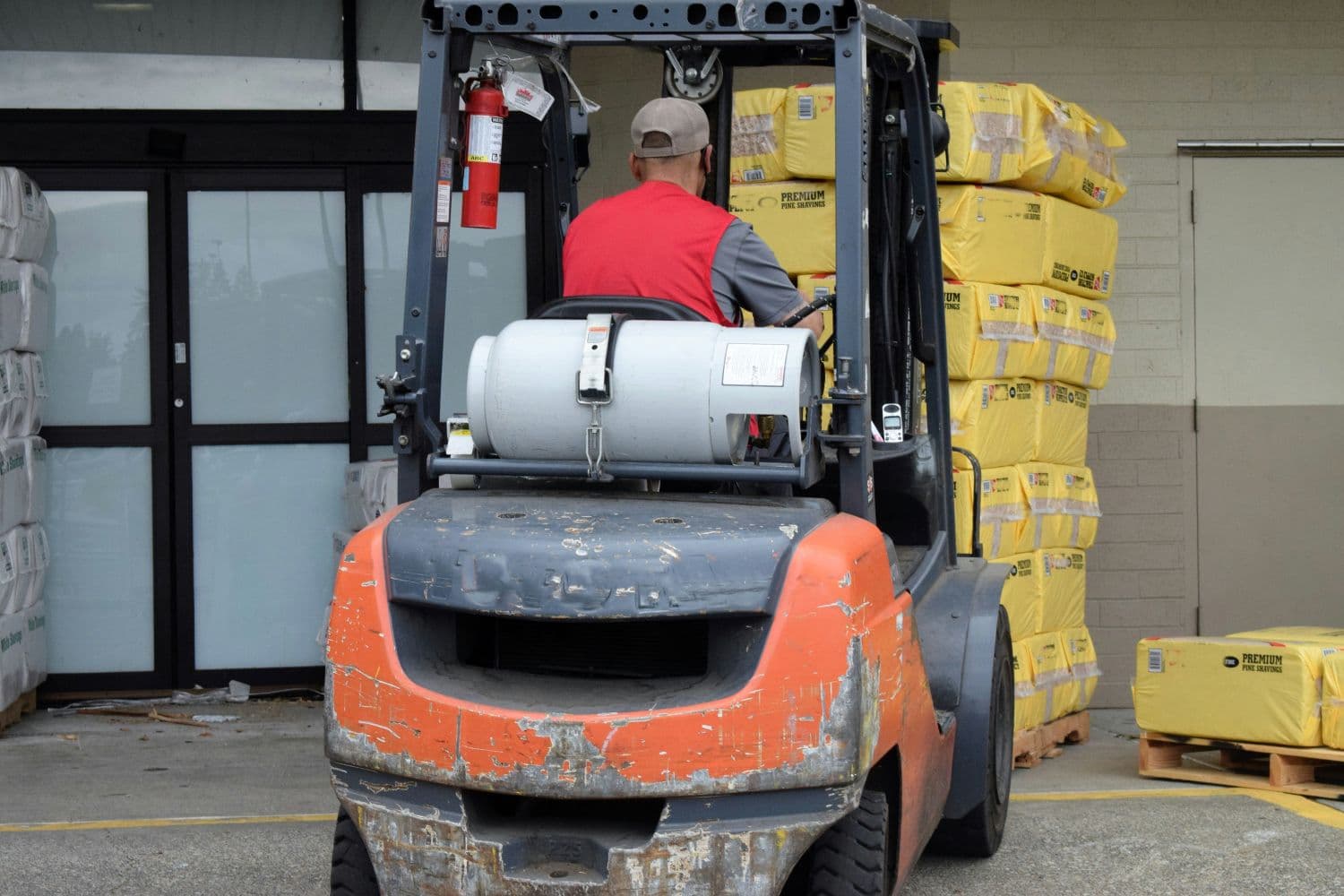 Forklift operator moving palletized products at a warehouse loading area.