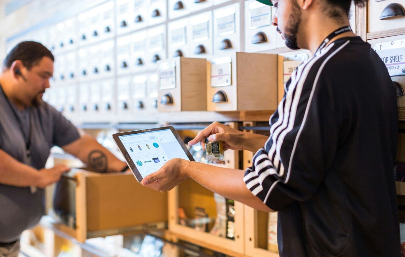 Two workers handling products and using a tablet in an inventory storage area.