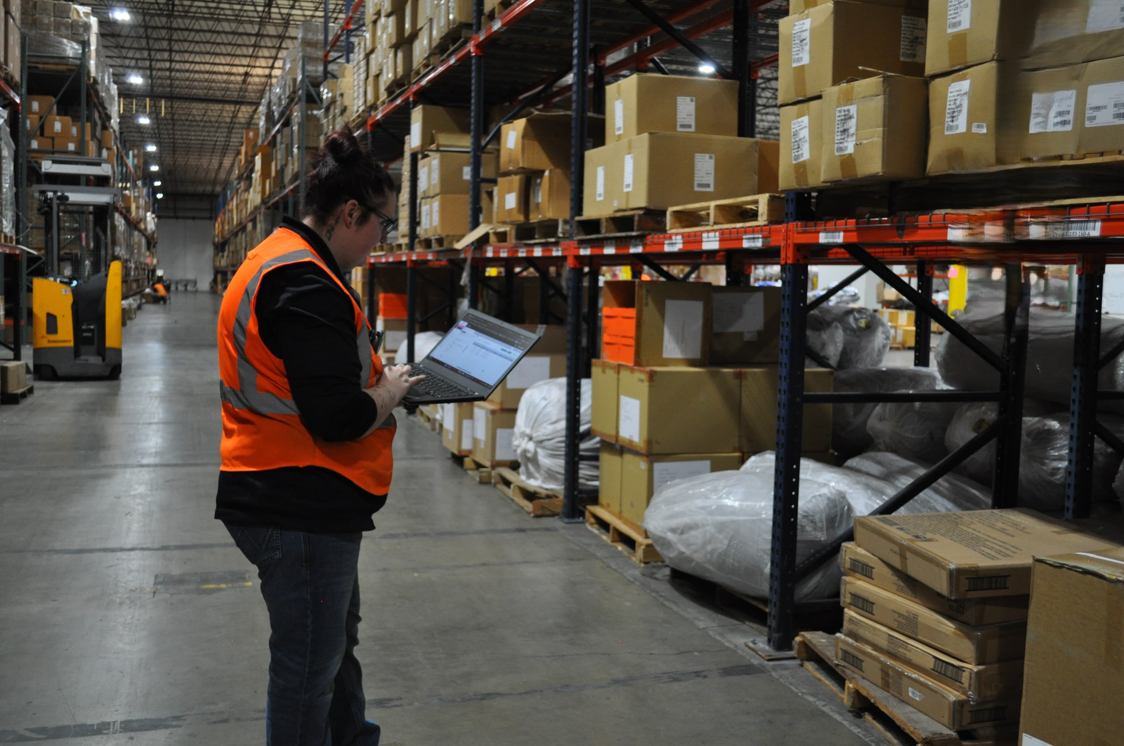 Fast Fulfillment employee using a laptop in a warehouse aisle with storage racks and boxes.