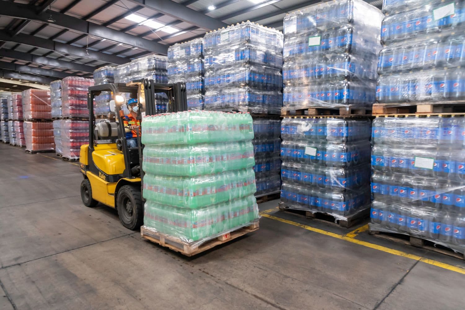 Forklift moving palletized bottled beverages inside a warehouse.